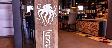 Un letrero de madera con un logotipo y el nombre 'eleftsch' en un interior moderno con una zona de bar.