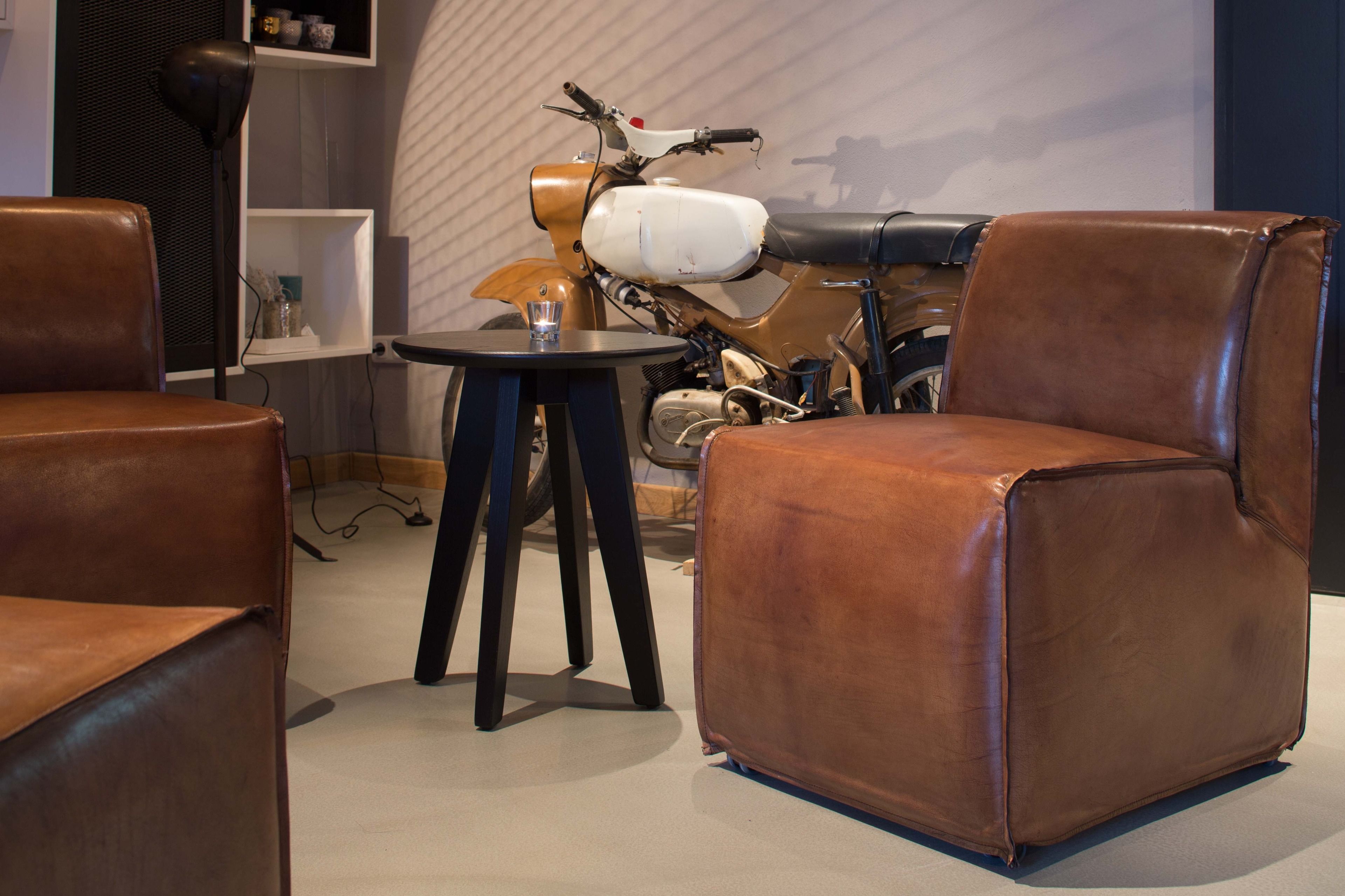 Een kamer met bruine leren stoelen, een klein rond tafeltje en een klassieke motor.