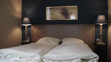 A double bed with white linens, two bedside lamps, a framed picture on the wall, and a small table with a clock on each side.