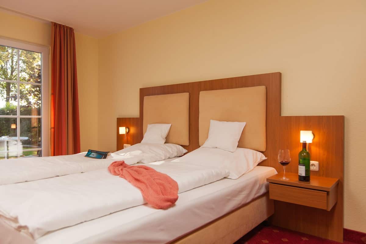 A double bed with white linens, two bedside tables with lamps, and a window with curtains.