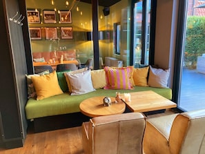 A cozy seating area with a green sofa, a wooden table, and a view of the outside. - Krögers Hotel (Esens)