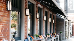 A covered outdoor seating area with benches and tables, large windows, and decorative lighting. - Krögers Hotel (Esens)