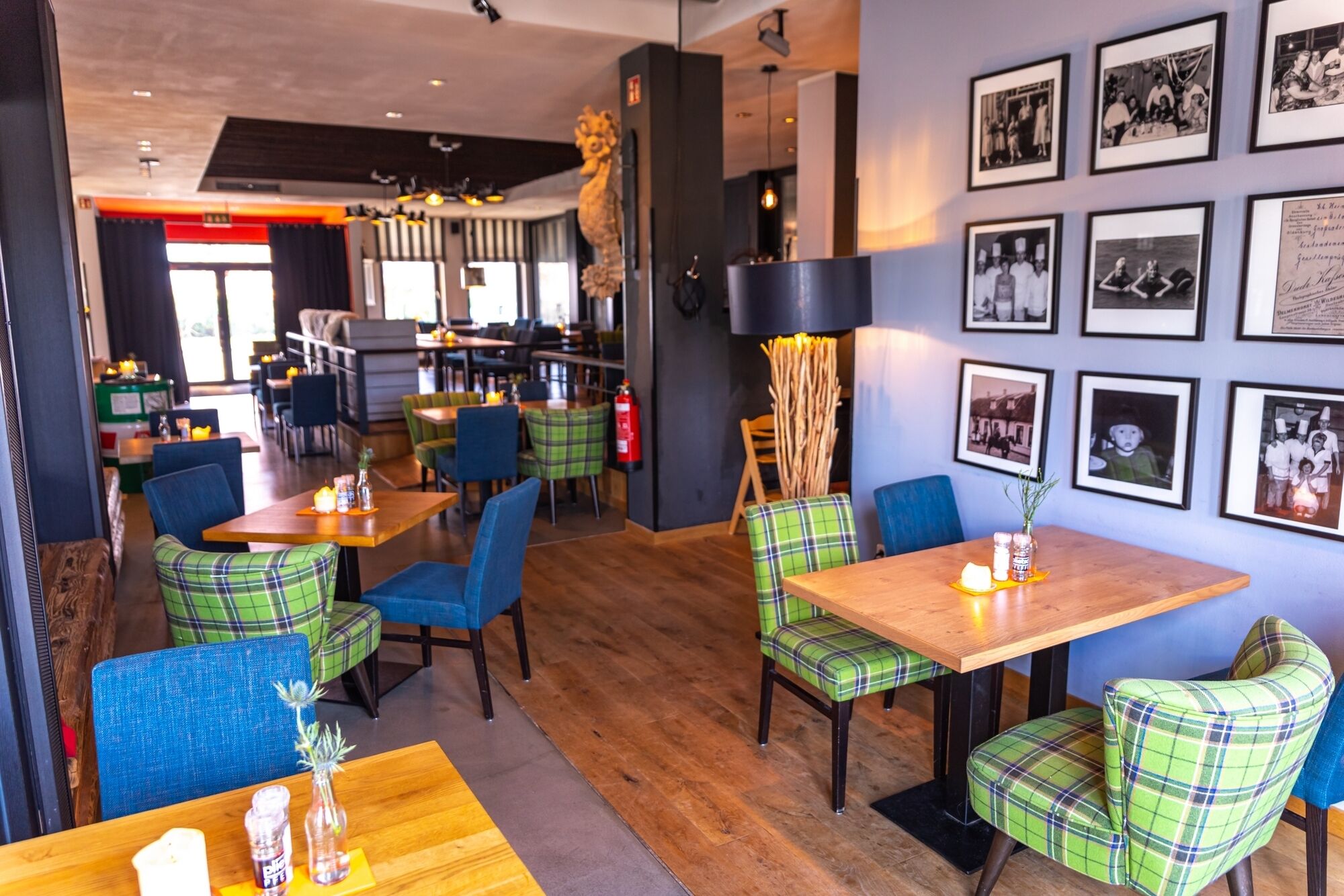 L’intérieur d’un restaurant est décoré de chaises à carreaux, de tables en bois et de photographies en noir et blanc accrochées aux murs.