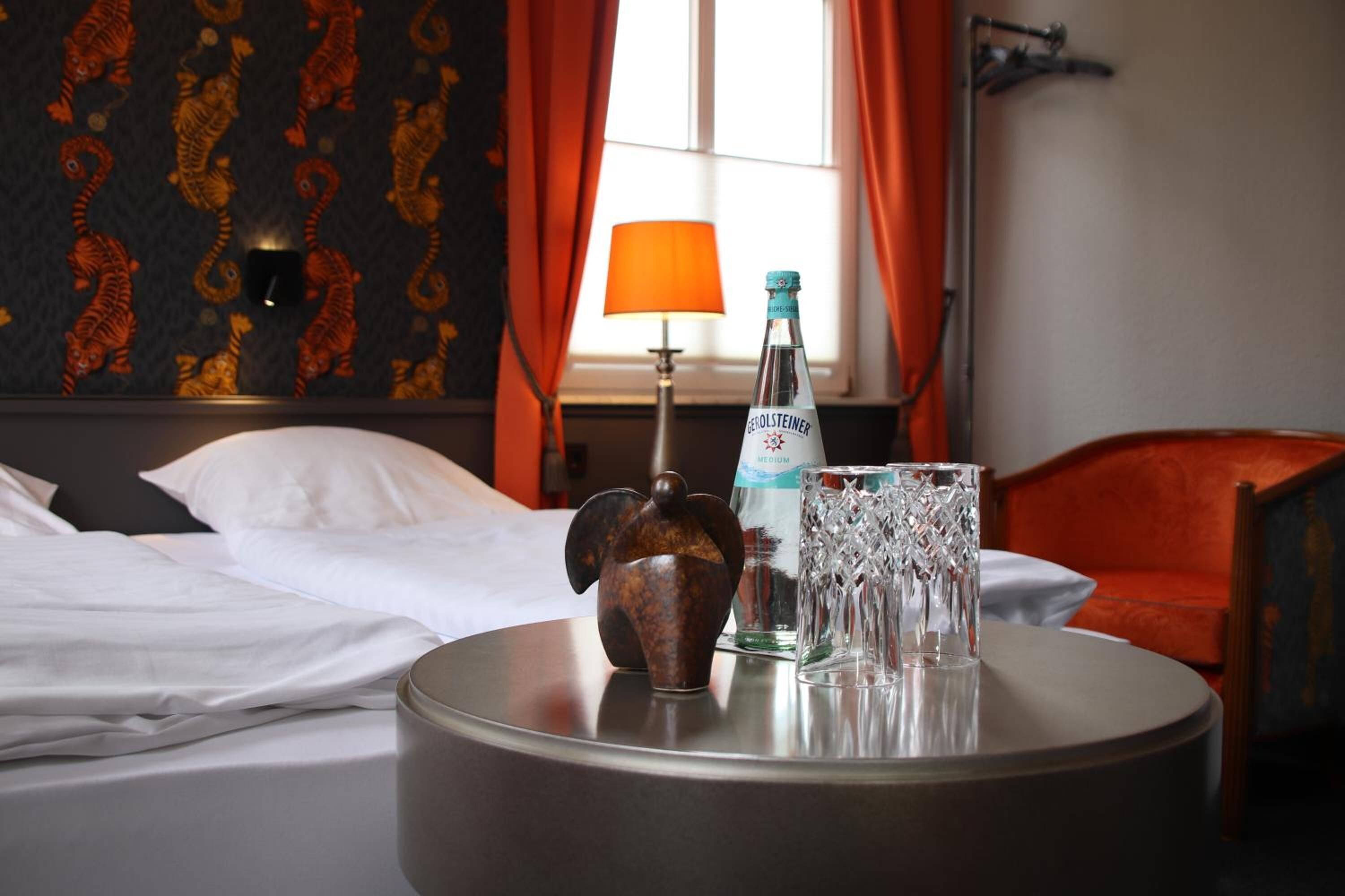 A hotel room with a bed, a round table with a bottle, a glass, and a decorative item.