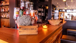 A bar area with a wooden counter, a bottle of Costa Rica rum, and various bottles in the background. - Krögers Hotel (Esens)