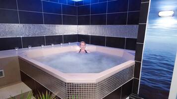 Un jacuzzi en una habitación con paredes de baldosas oscuras y un ventanal con vista al mar.