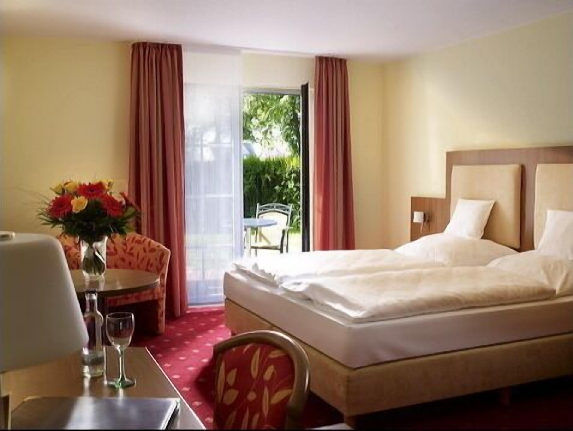 Habitación de hotel con una cama, un escritorio con un florero y vistas al exterior.