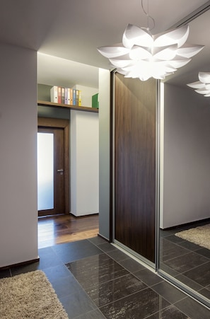 A modern hallway with a wooden door, a mirror, and a white flower-shaped light fixture. - Apartament ST1 (Cieszyn)