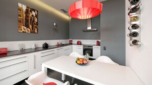 A modern kitchen with white cabinetry, a central island with seating, a red pendant light, and a wine rack on the wall. - Apartament ST1 (Cieszyn)
