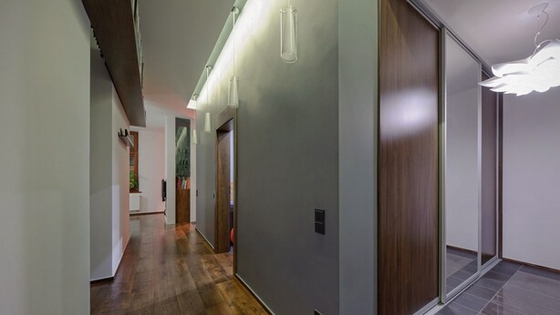 A modern hallway with wooden flooring, a sliding door, and a wall-mounted light fixture. - Apartament ST1 (Cieszyn)