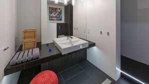 A modern bathroom with a large mirror, white sink, dark tiles, and a red pouf. - Apartament ST1 (Cieszyn)