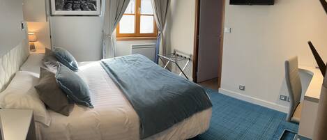 A hotel room with a bed, a desk, a chair, a TV, and a window with curtains.