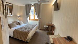 Una habitación de hotel con cama, escritorio, silla, televisor y ventana con cortinas.
