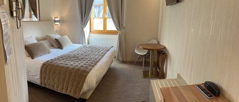 Una habitación de hotel con cama, escritorio, silla, televisor y ventana con cortinas.