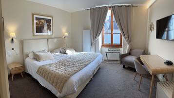 A hotel room with a large bed, a desk, a chair, a TV, and a window with curtains.