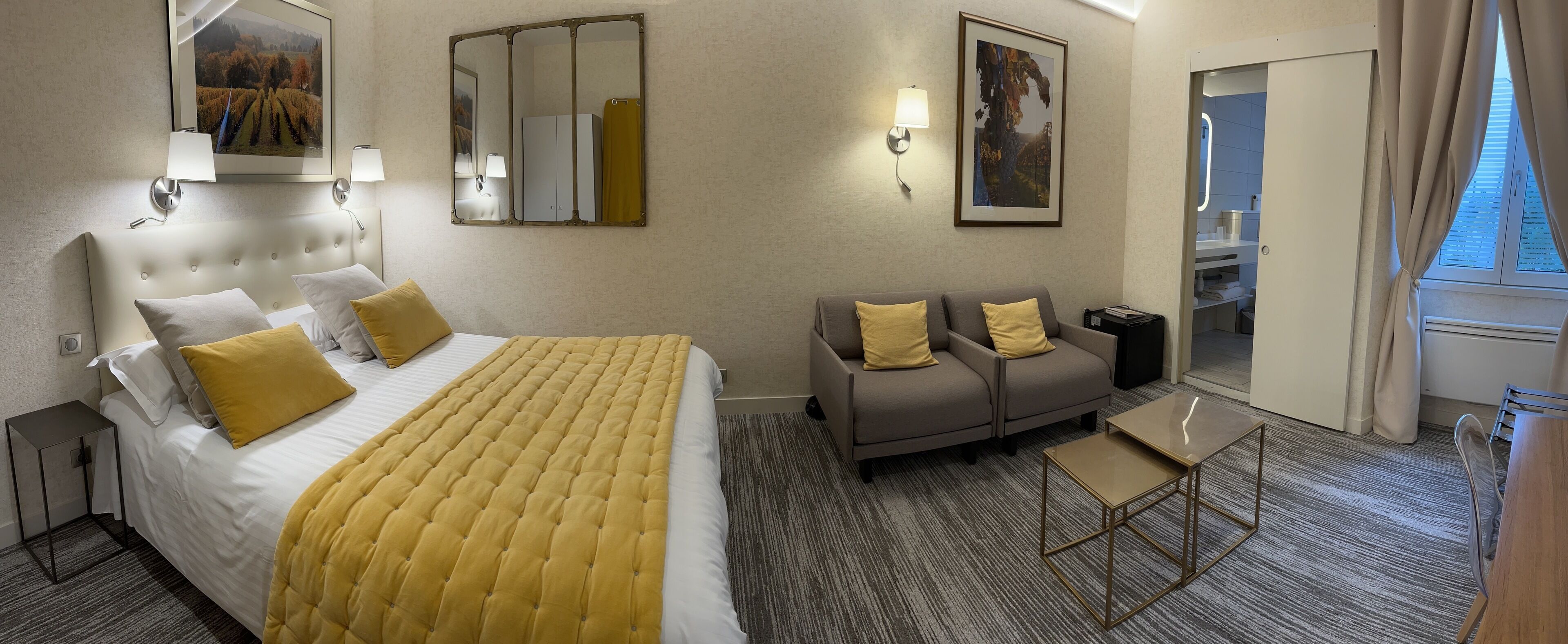 Una habitación de hotel con cama, sofá, mesita y espejo.