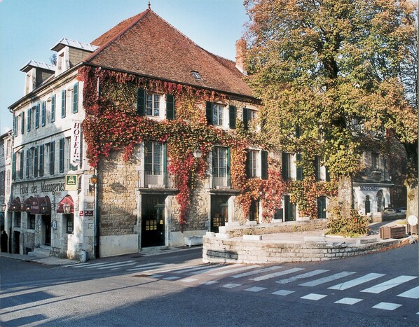 A historic building with a stone facade, green shutters, and a red-tiled roof. - Hotel des Messageries (Arbois)