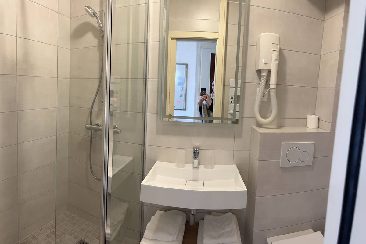 Ein modernes Badezimmer mit einer gläsernen Duschkabine, einem weißen Waschbecken und einem Spiegel darüber.
