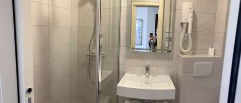 Un baño moderno con cabina de ducha de vidrio, lavamanos blanco y espejo superior.
