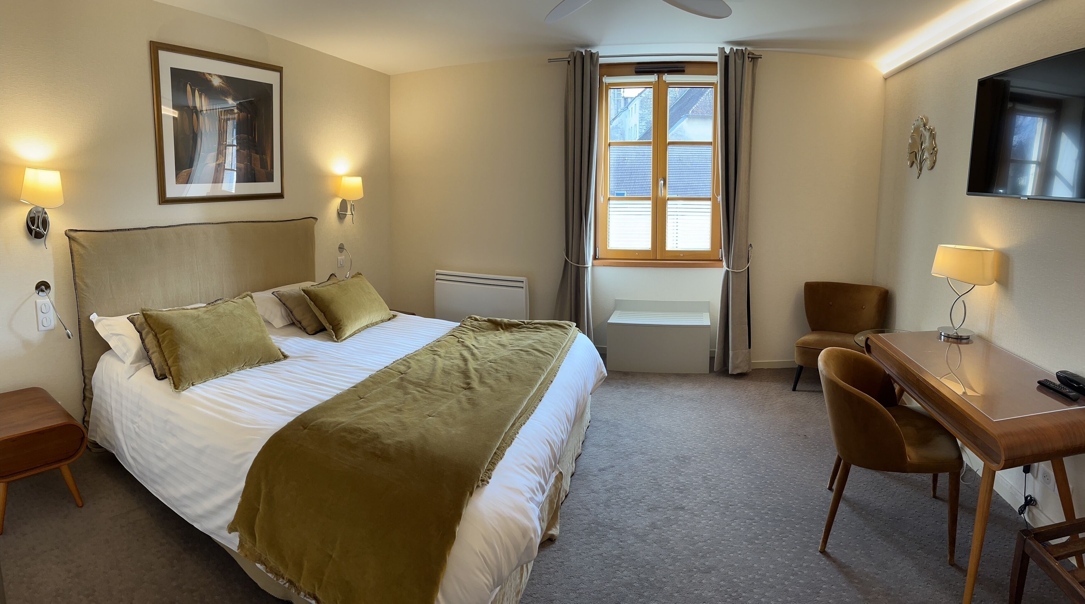 Et hotelværelse med seng, skrivebord, stol, fjernsyn og et vindue med gardiner.