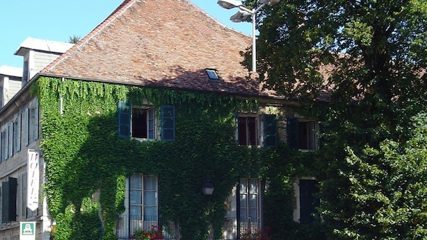 Un edificio histórico con un techo empinado, muros cubiertos de hiedra y una fachada tradicional.