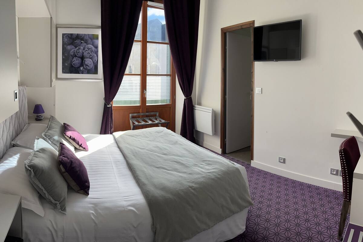 Ein Hotelzimmer mit Bett, Schreibtisch, Stuhl, Fernseher und einem fenster mit Vorhängen.