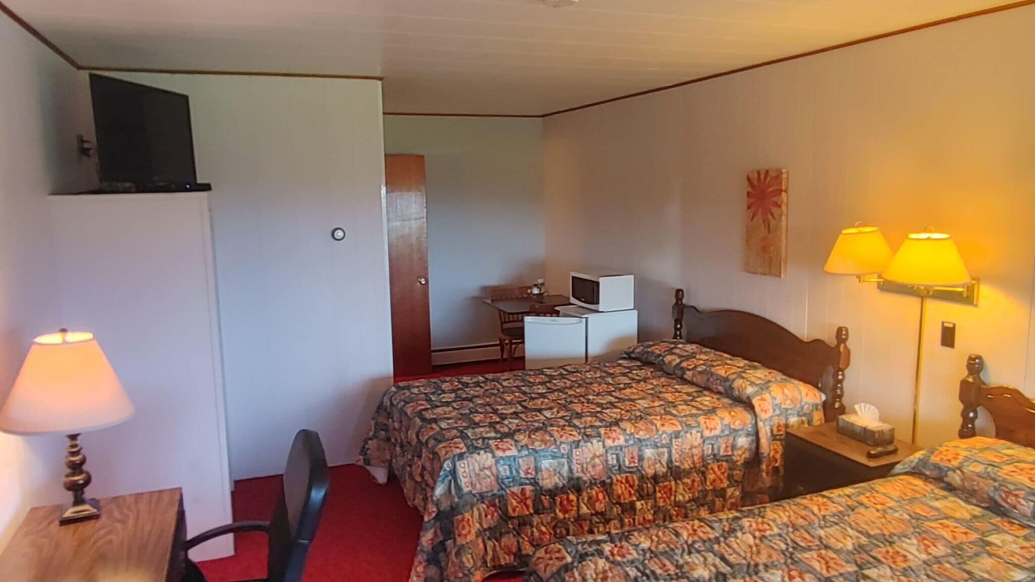 A hotel room with two beds, a desk, a chair, a TV, and a desk lamp.