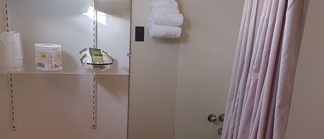 Baño con inodoro, lavamanos y bañera. Hay toallas y artículos de aseo en estantes.