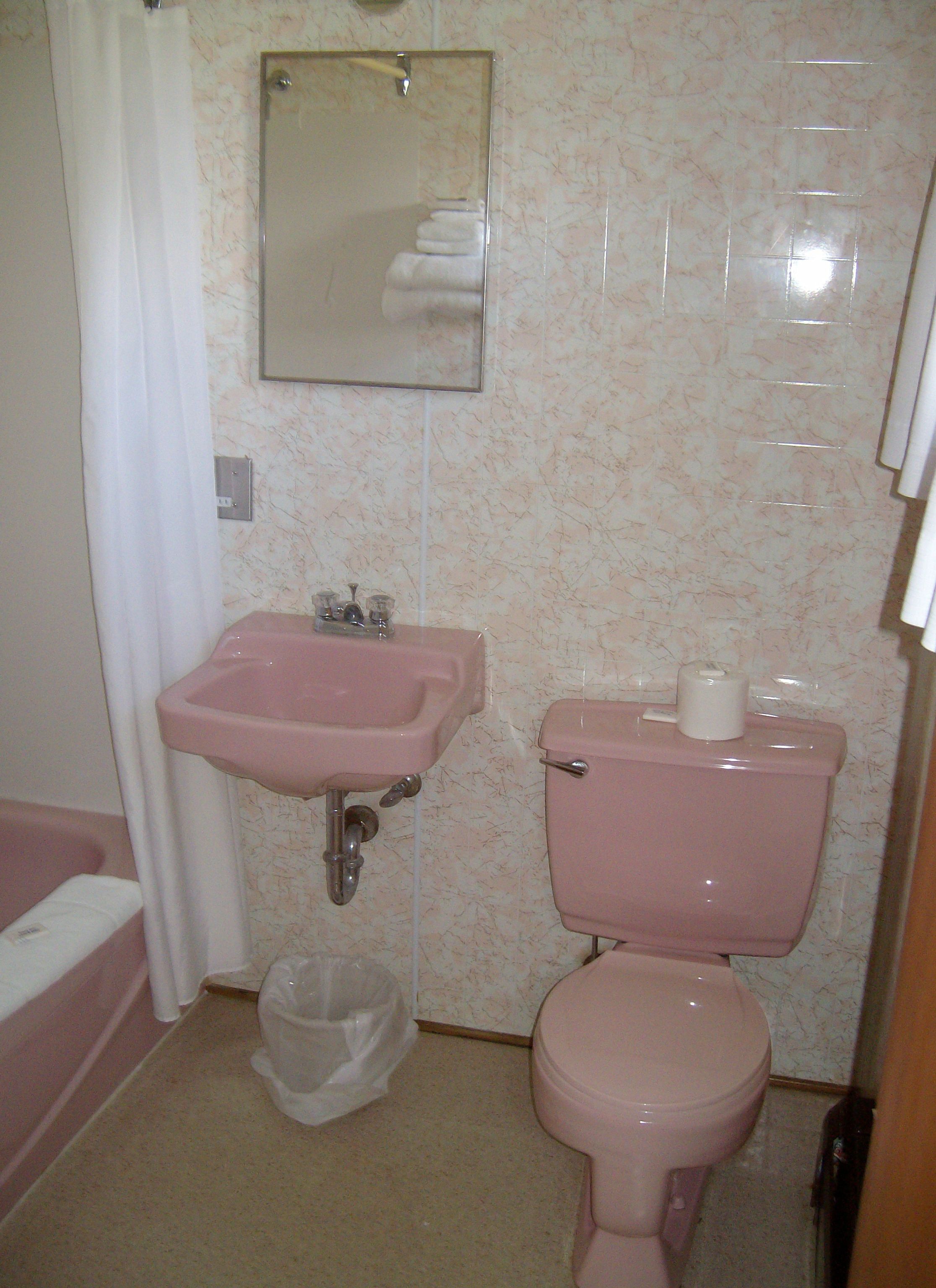 Une salle de bain avec un lavabo, des toilettes et une baignoire, le tout de couleur rose.