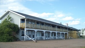 A two-story building with a balcony on the upper floor, a covered porch with chairs, and a gravel driveway. - Singing Sands Inn Motel (Kingsboro)