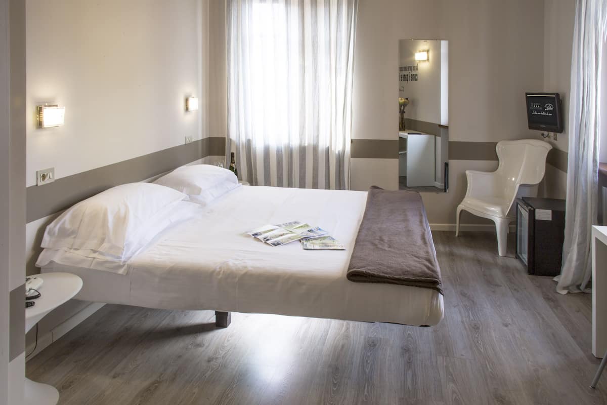 A hotel room with a large bed, bedside table, and a desk with a chair.