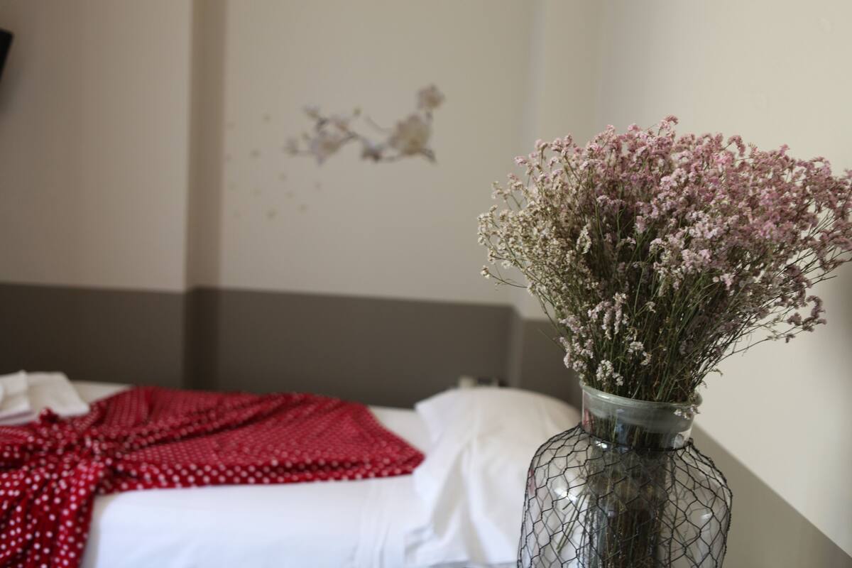 A bed with a red polka dot blanket and a vase of flowers on a bedside table.