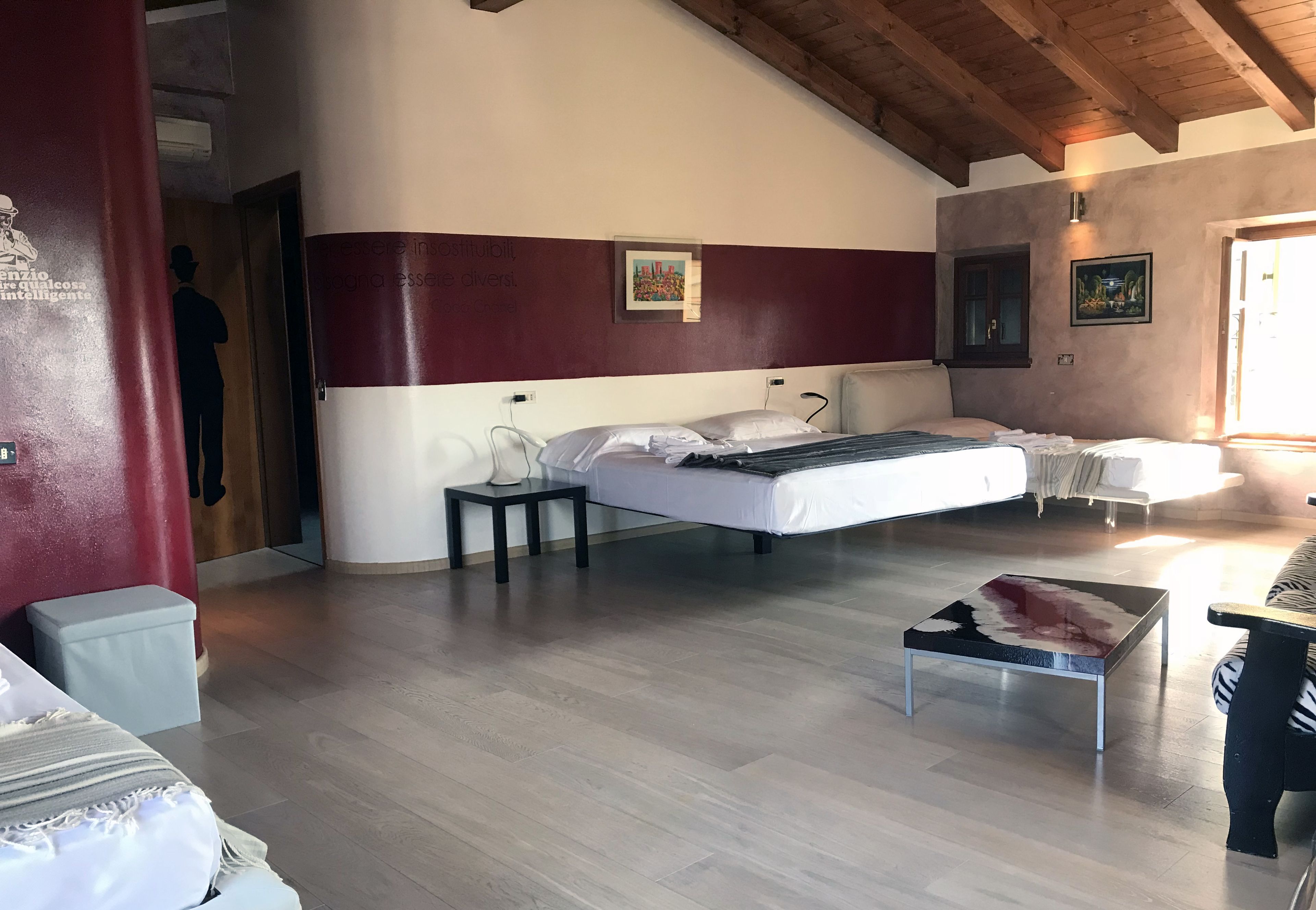 A bedroom with a bed, bedside tables, a wooden floor, and a red accent wall.