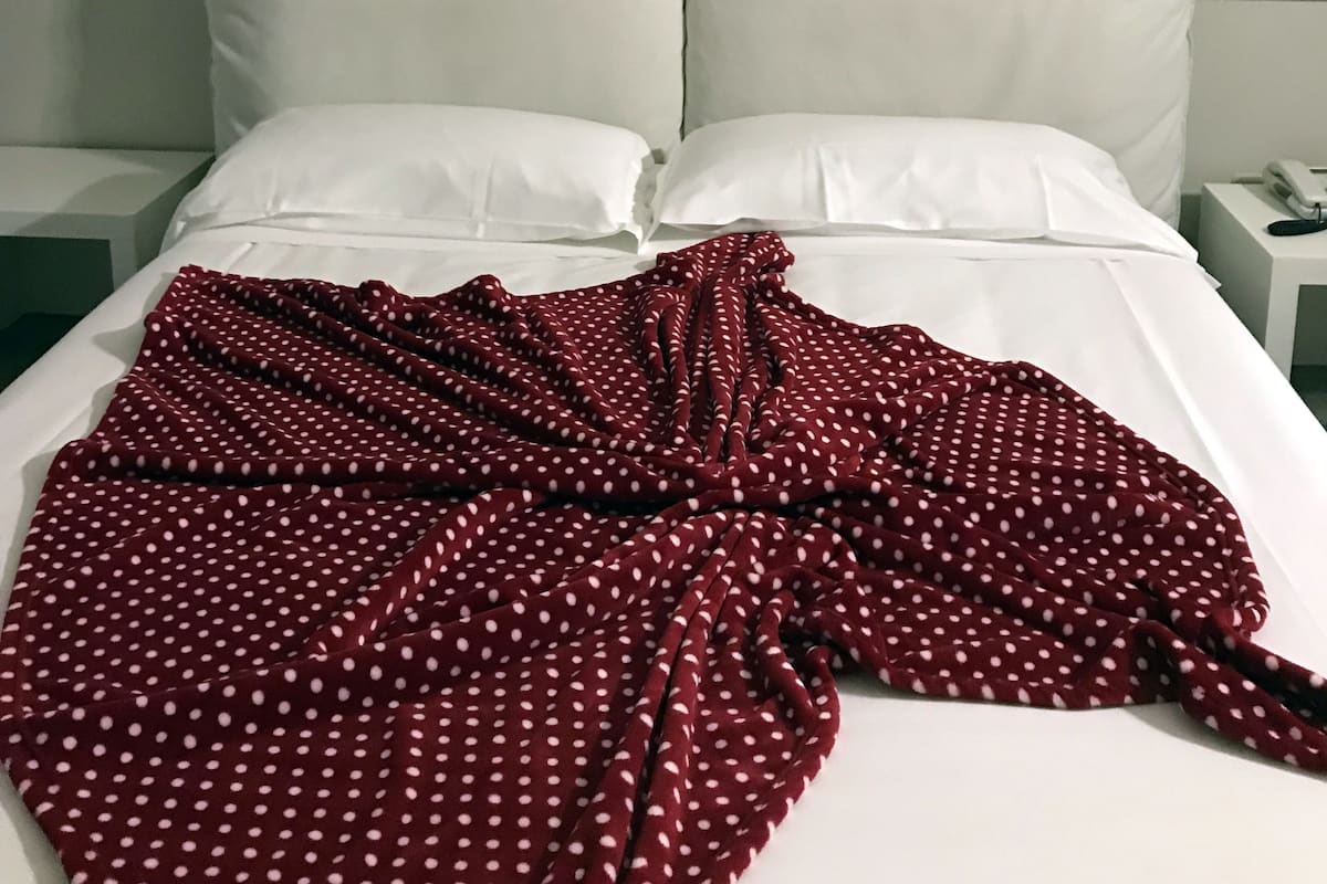 A hotel room with a bed, white bedding, a red polka dot blanket, and a wall with large text reading "genius" and "Aristotle".