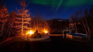 A person sitting by a pool at night with a view of the northern lights. - Hotel Kjarnalundur (Akureyri)