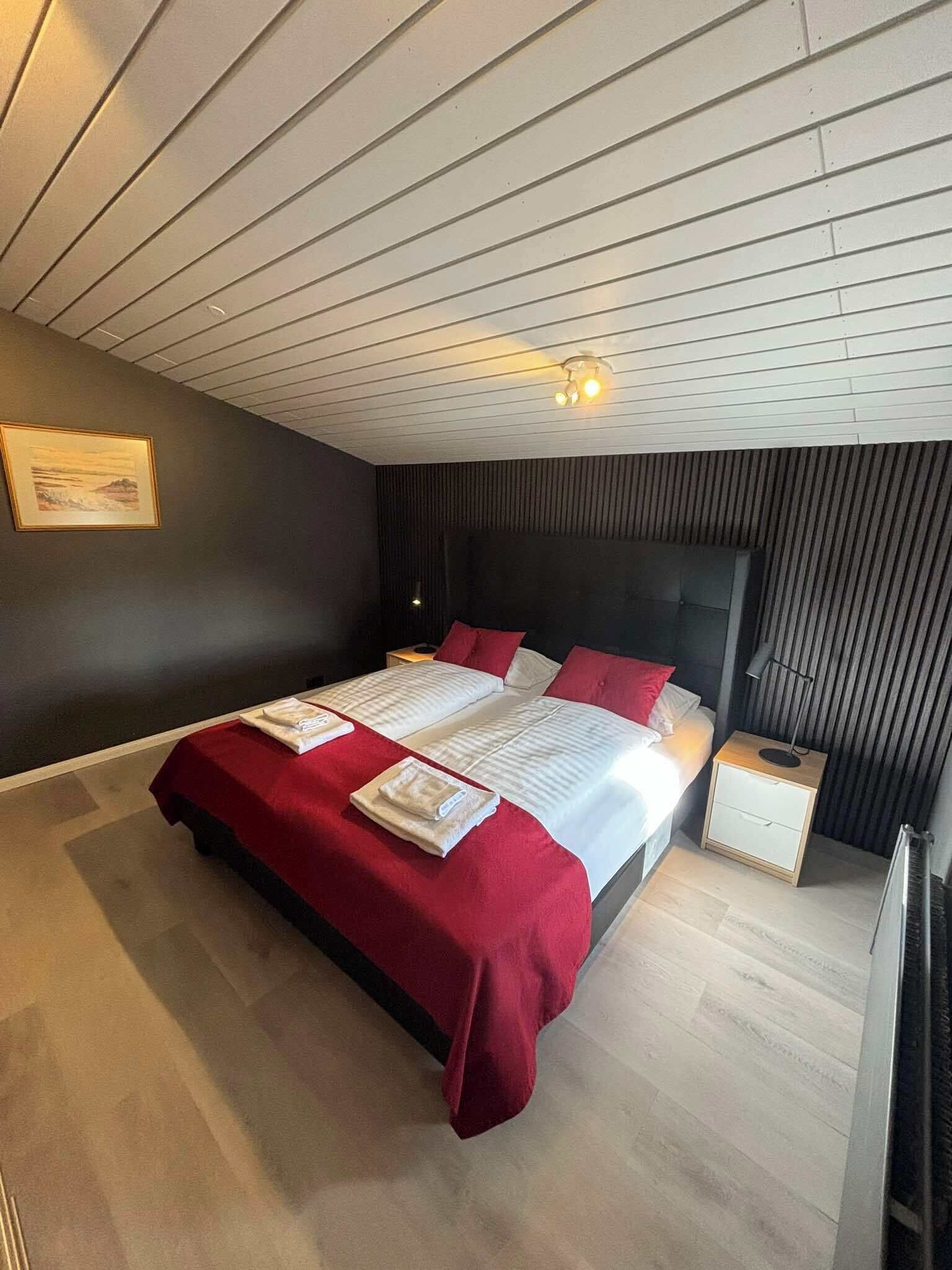 A modern bedroom with a large bed, a nightstand, a wall-mounted lamp, and a framed picture on the wall.