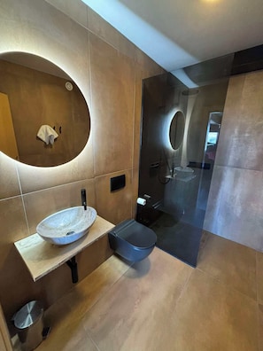 A modern bathroom with a large oval mirror, a vessel sink, a black toilet, and a glass-enclosed shower area.