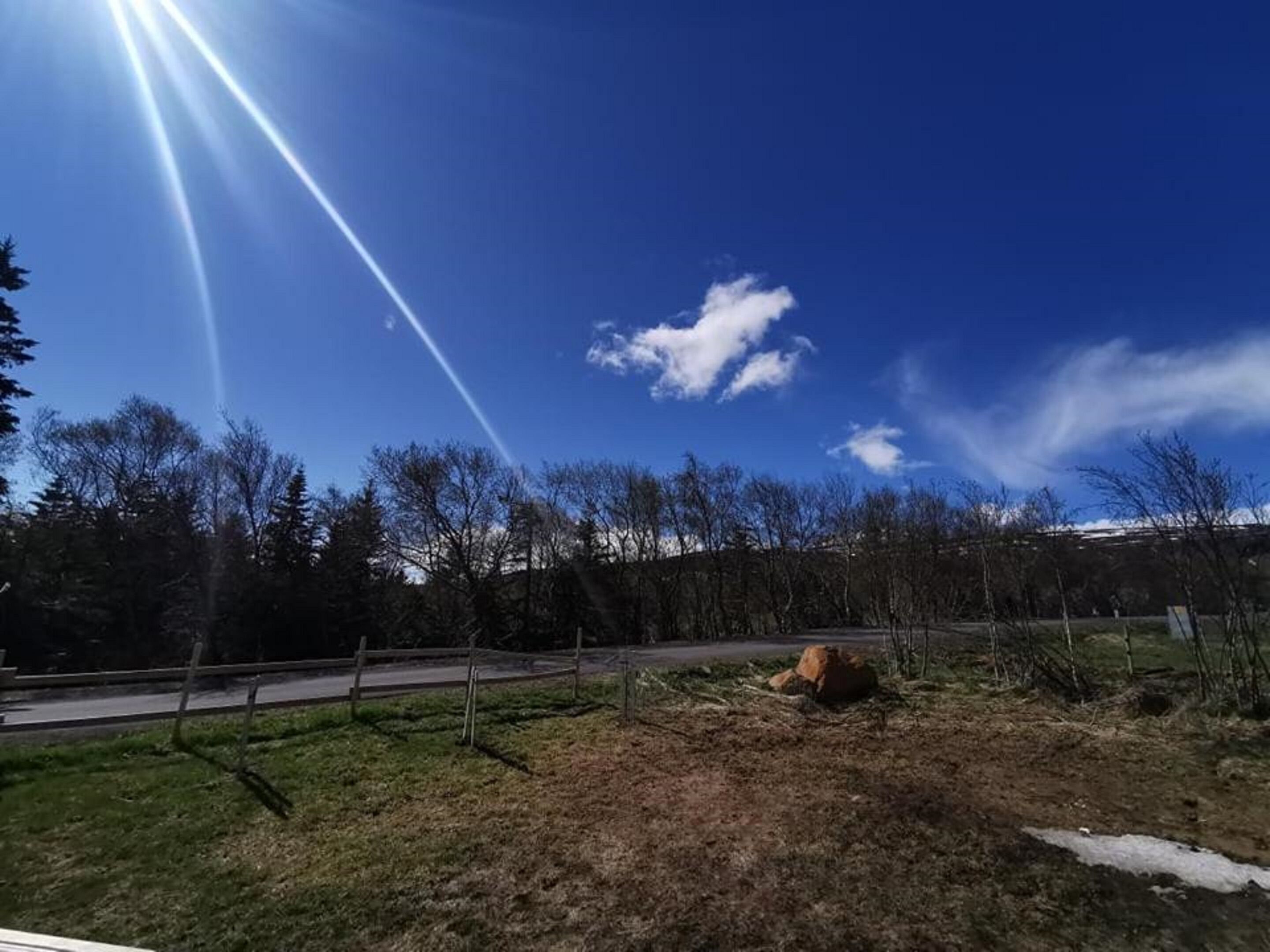 A clear sky with a contrail, a road, and a grassy area with trees.