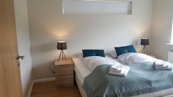 Un dormitorio con dos camas, una mesita de noche, una lámpara y una ventana.