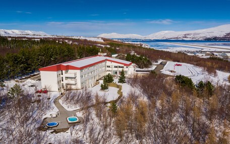 A large building with a red roof, surrounded by snow-covered landscape and trees.