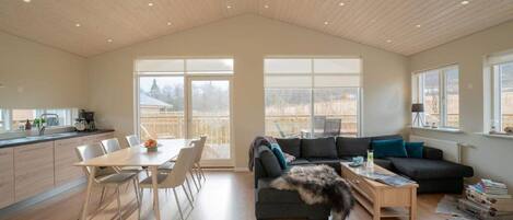 A spacious living area with a dining table, a sofa, and a large window offering a view of the outdoors.