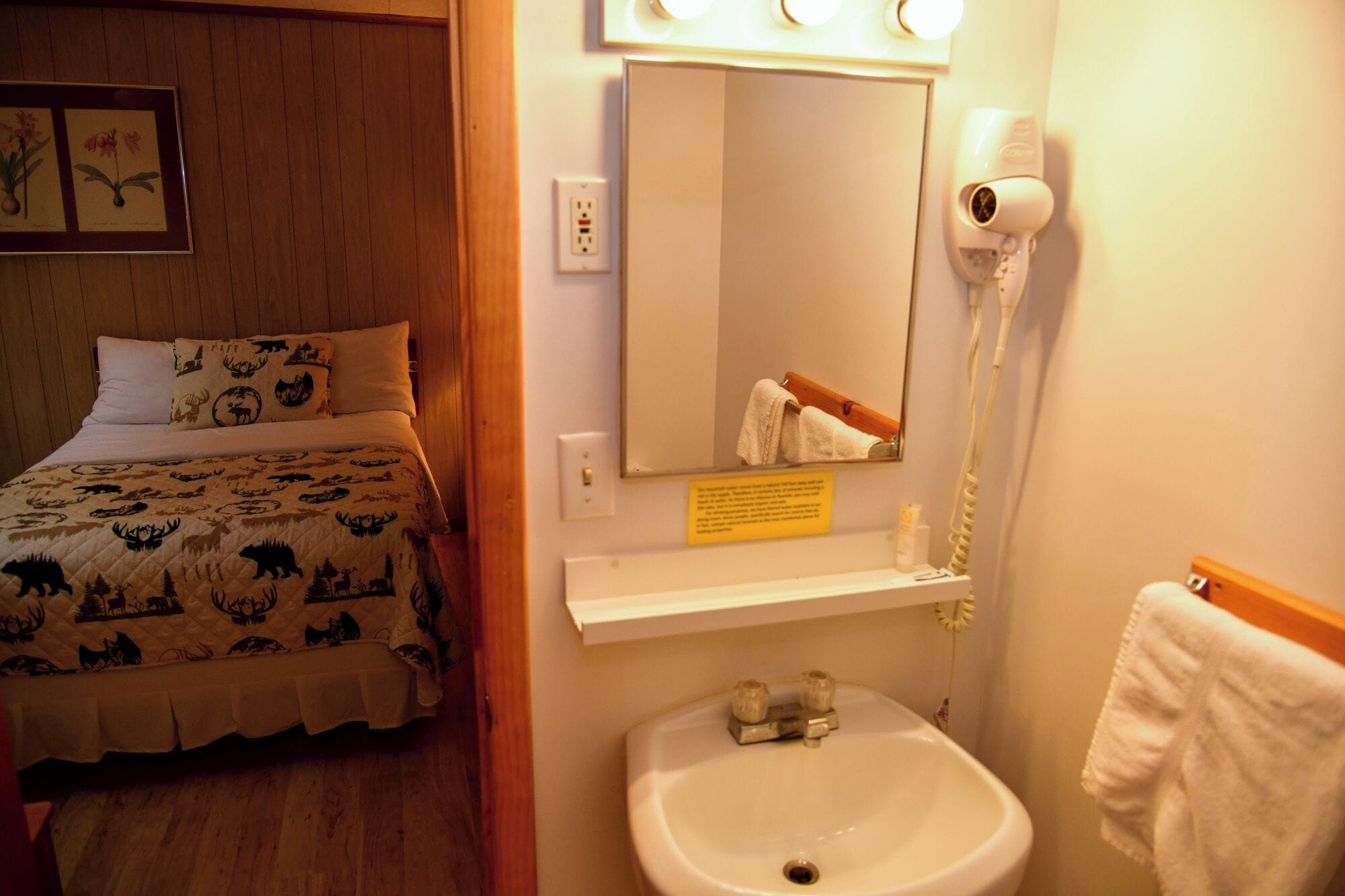 Una camera d'albergo con un letto, uno specchio, un asciugacapelli e un lavandino.