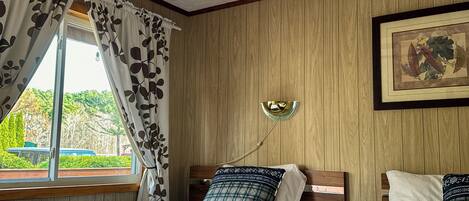 A bedroom with two beds, wooden panel walls, a skylight, and a window with curtains.