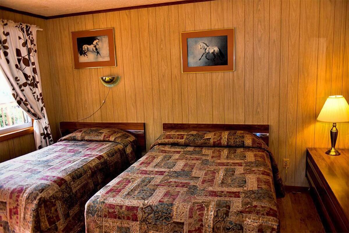 Ein Zimmer mit zwei Betten, Holzwandverkleidung, einem Fenster mit Vorhang und zwei gerahmten Bildern an der Wand.