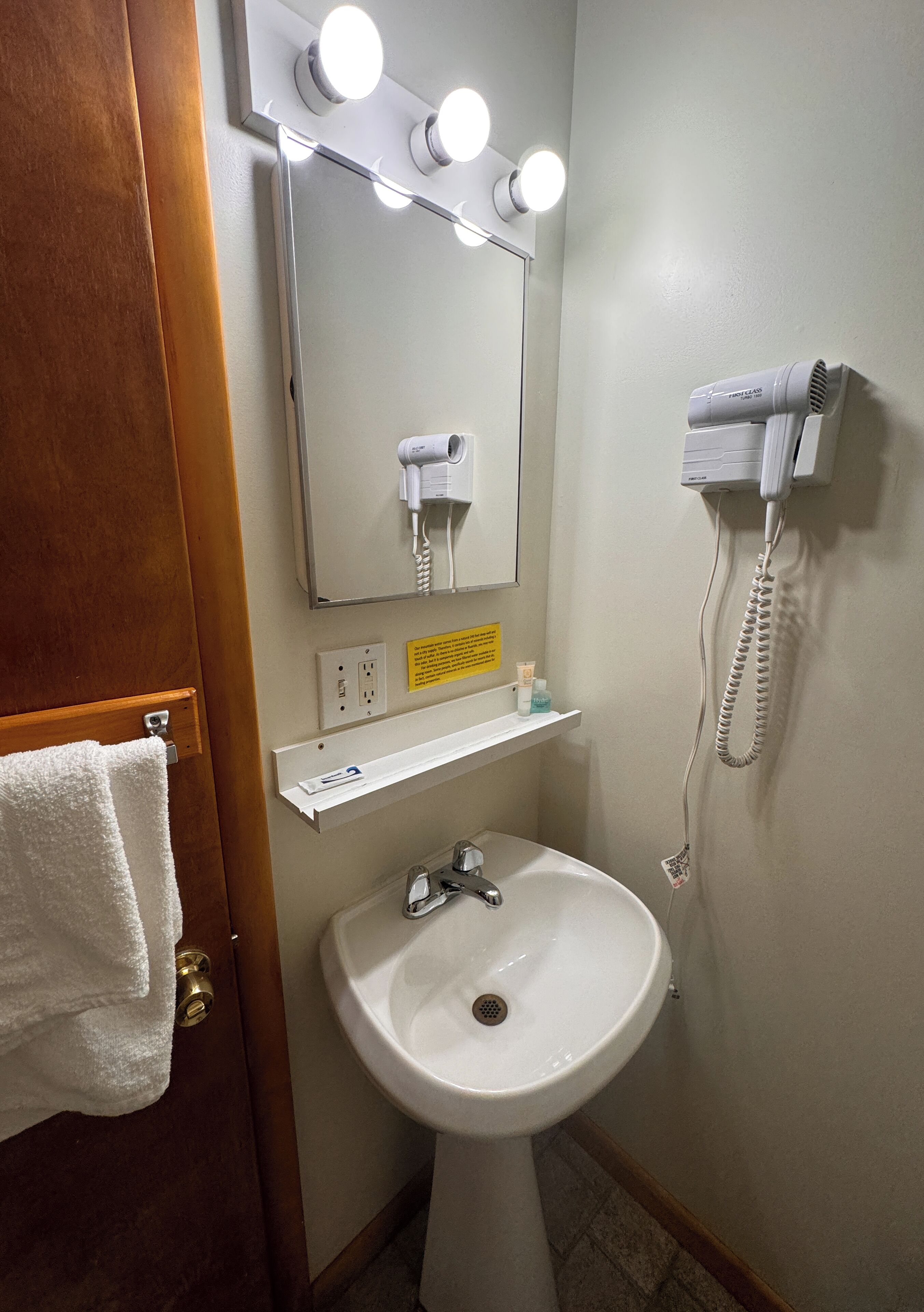 A bathroom with a sink, mirror, hairdryer, and a towel rack.