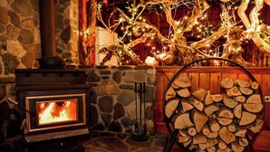 Una chimenea de piedra con fuego a la vista, un montón de leña y luces decorativas.