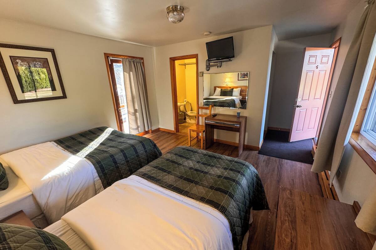 Ein Hotelzimmer mit zwei Betten, einem Schreibtisch, einem Sessel, einem Fernseher und einem durch eine geöffnete Tür einsehbaren Badezimmer.