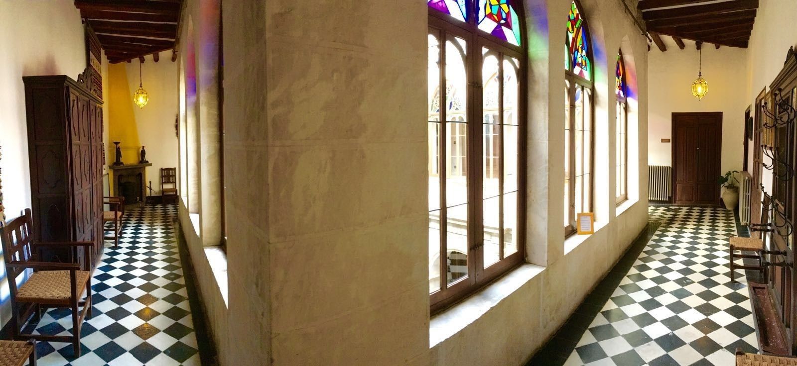 A corridor with checkered flooring, wooden benches, and stained glass windows.