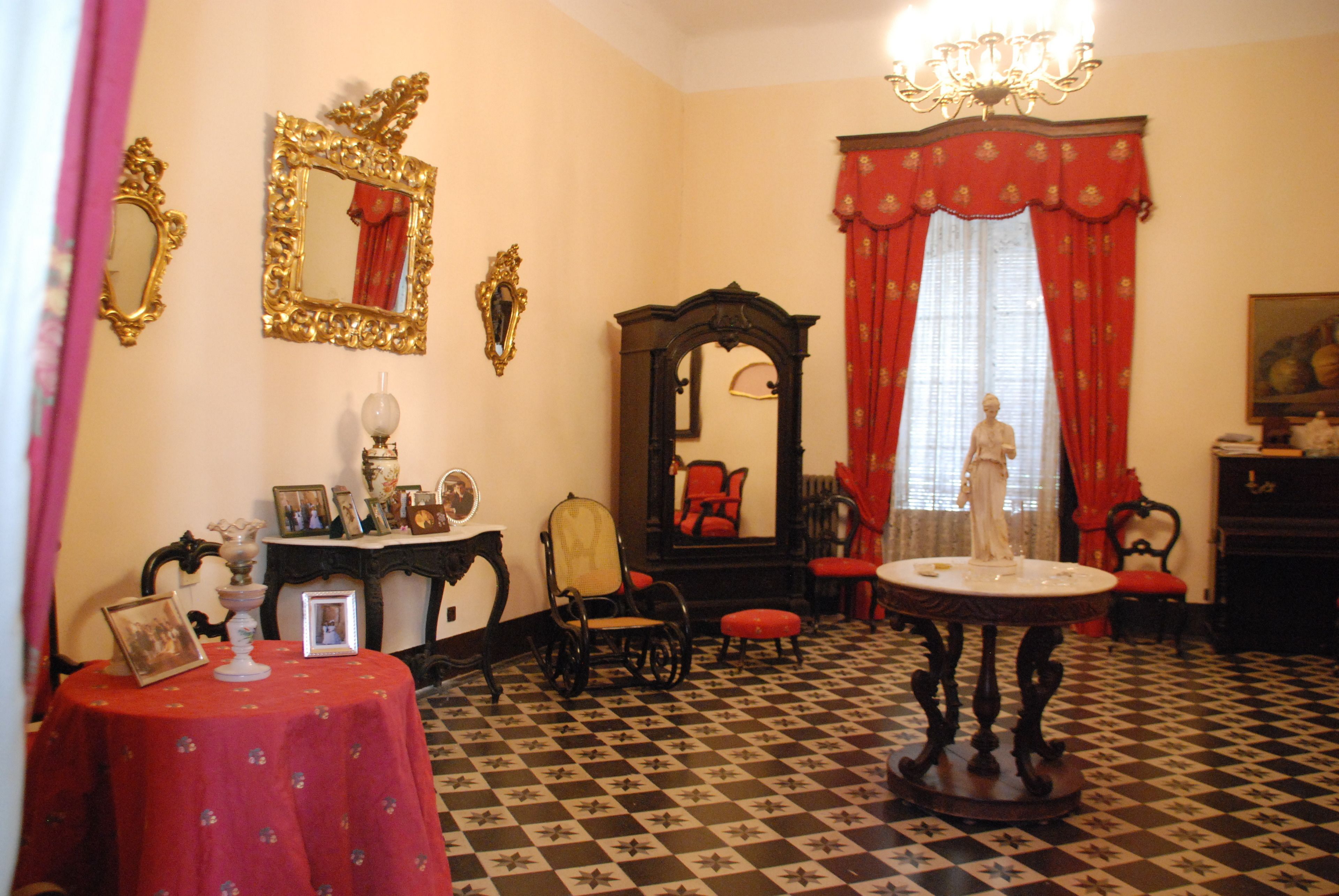 Una habitación con piso a cuadros, una mesa con mantel rojo, una silla, un espejo y una estatua.