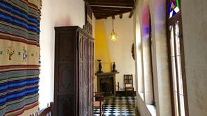 Un pasillo con suelo de tablones, un armario de madera, una lámpara colgante y un ventanal con vitrales.
